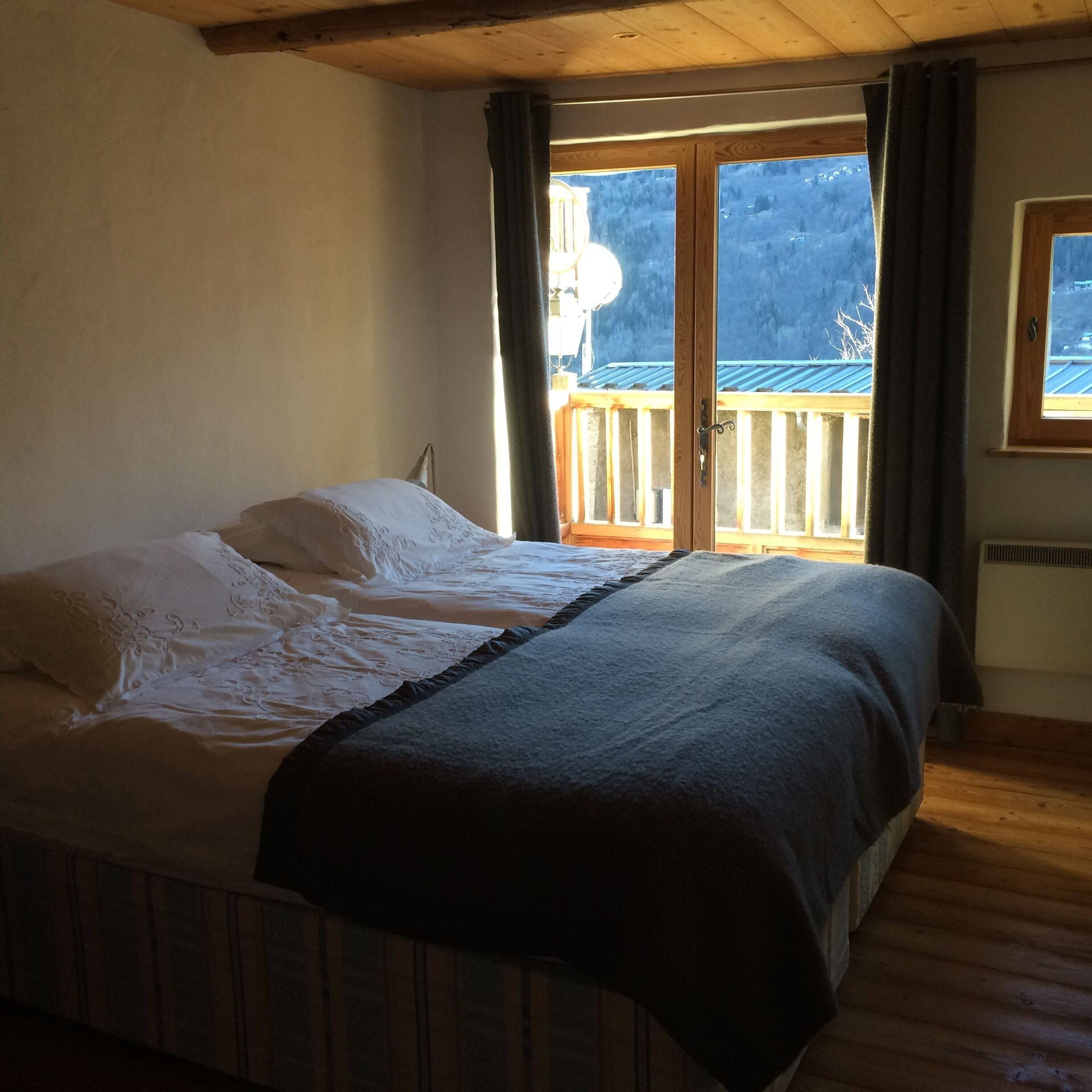 Et soveværelse med seng, træloft, et vindue og udsigt til en balkon.