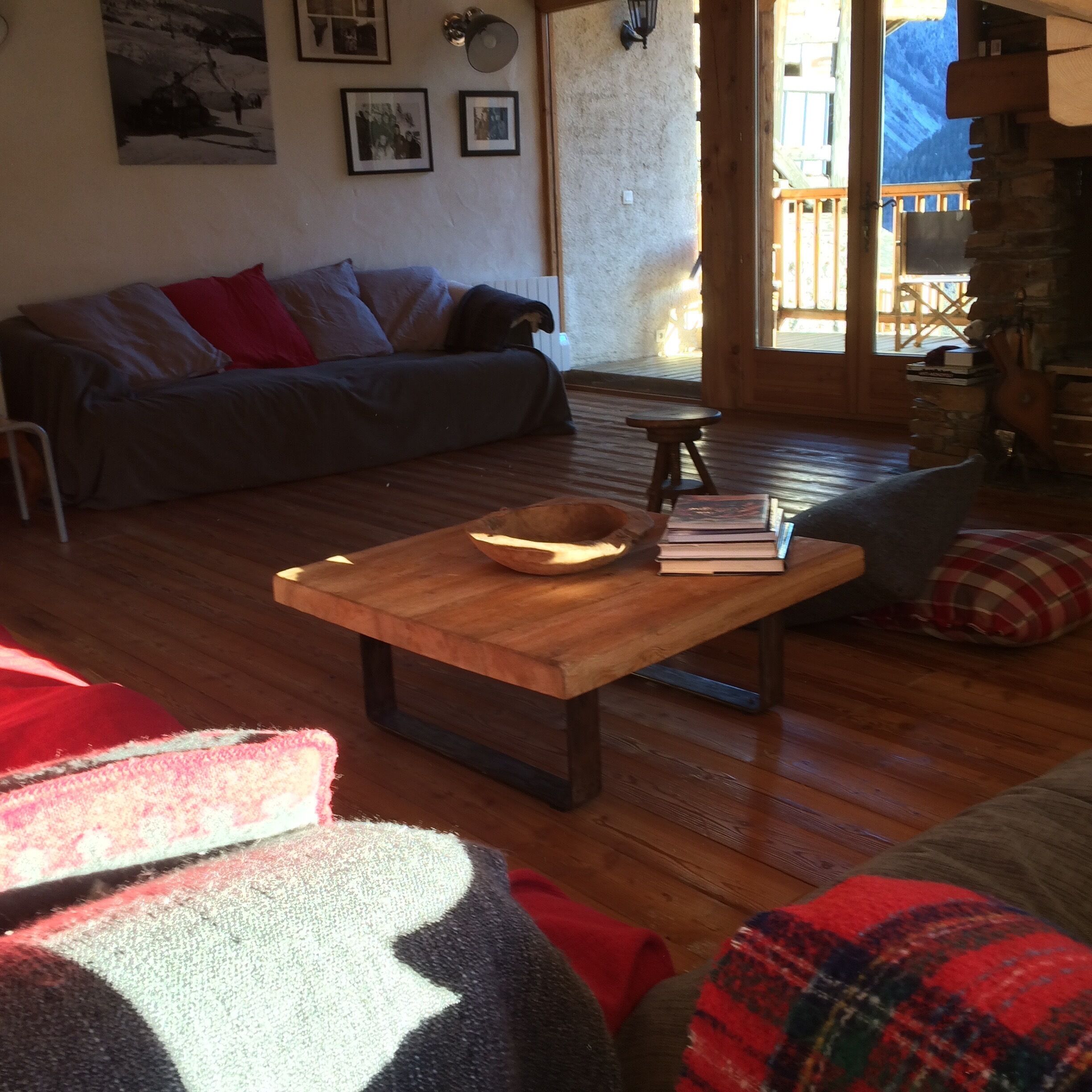 A cozy living room with a wooden coffee table, a sofa, and a view of a wooden deck through a glass door.
