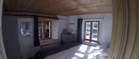 Un dormitorio con techo de madera, una cama con ropa de cama blanca, una ventana con cortinas y un aparador.
