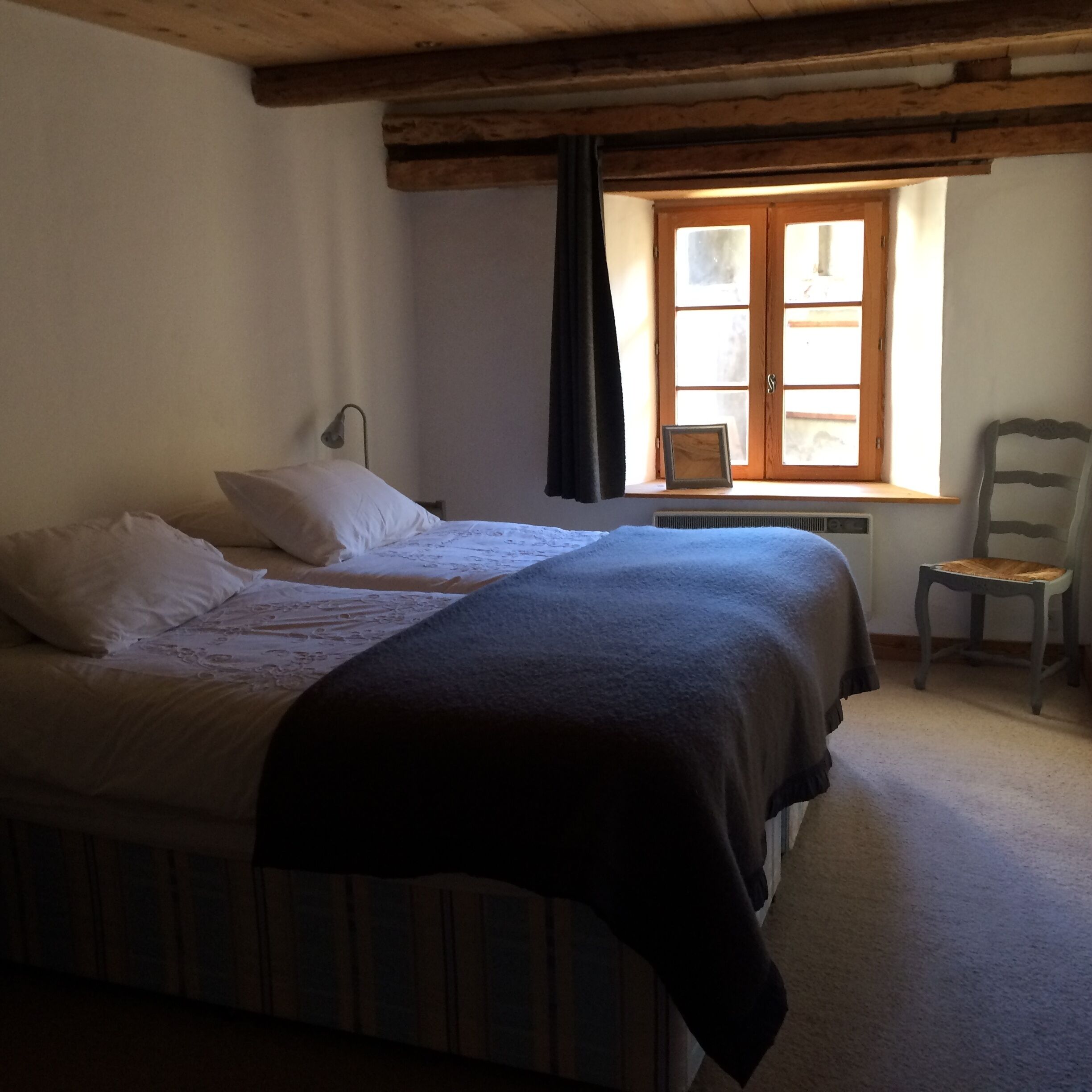 A bedroom with two beds, a window with curtains, a chair, and a radiator.