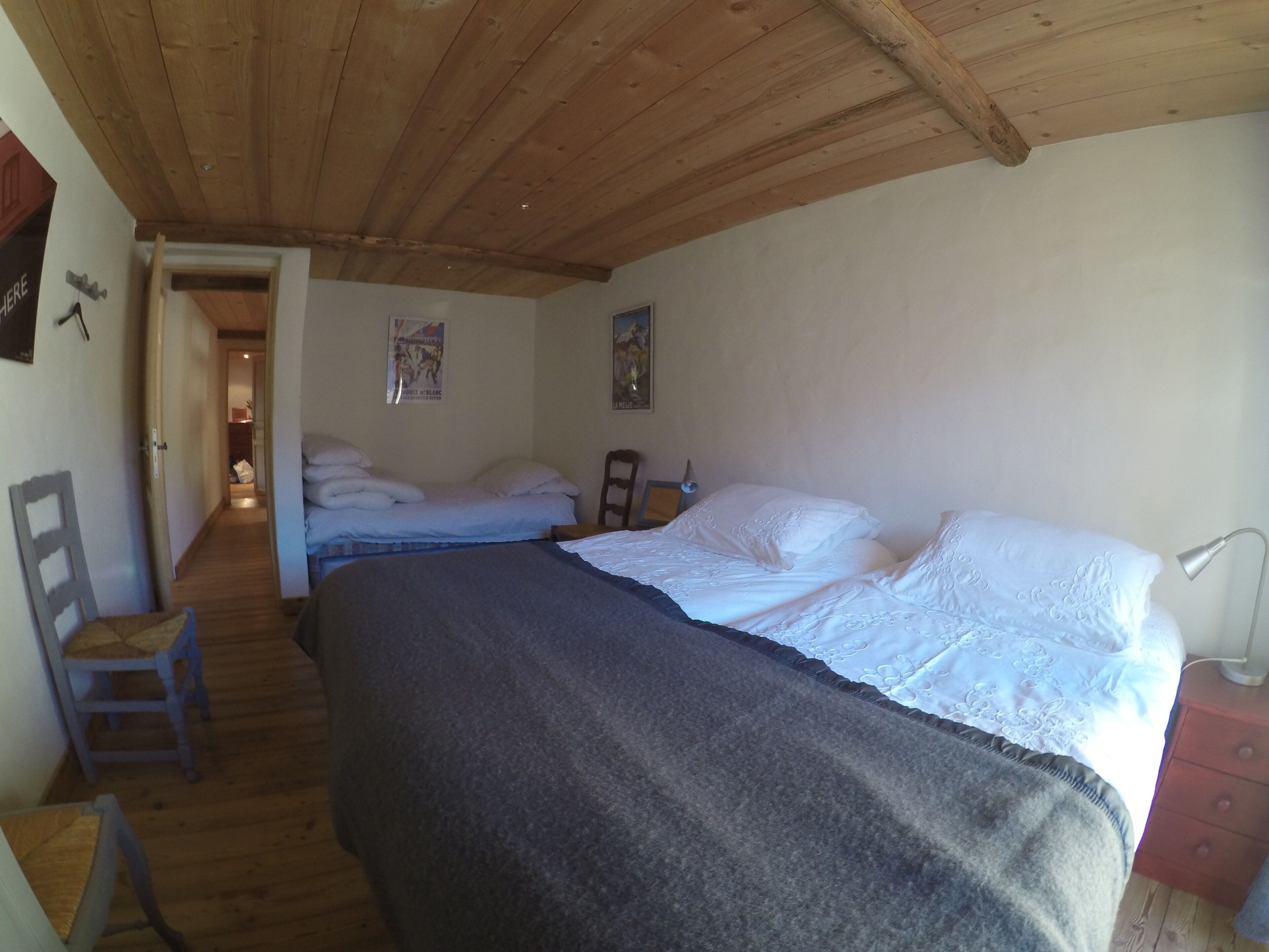Un dormitorio con dos camas, suelo de madera, techo de madera y un escritorio pequeño con una silla.