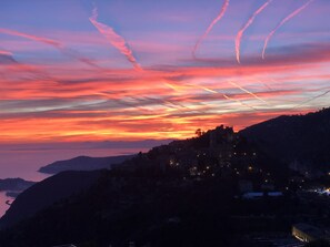Et kystlandskab ved solnedgang med silhuetter af en by og bjerge i baggrunden.
