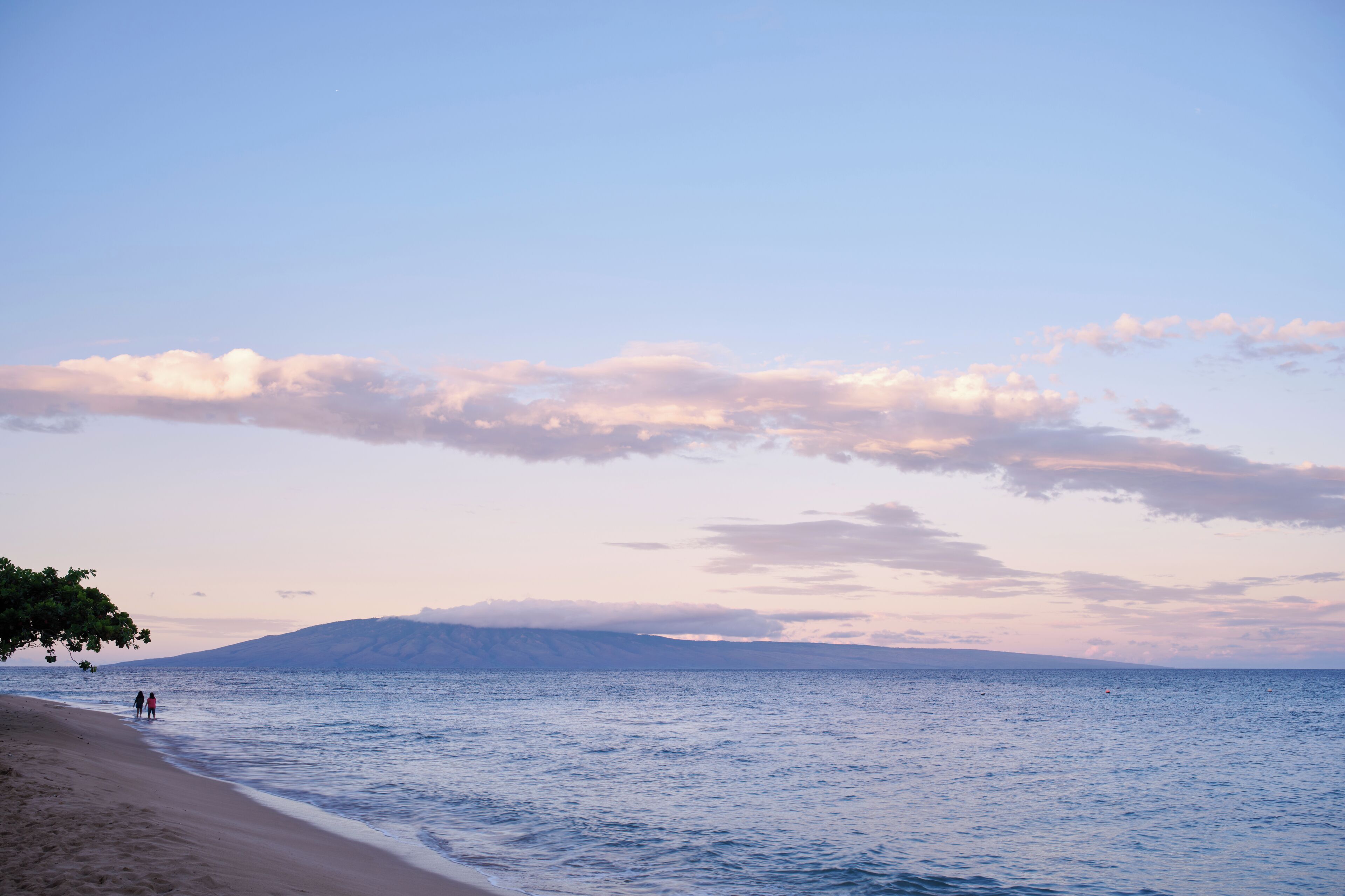 A beach with a clear sky, calm sea, and distant mountains.