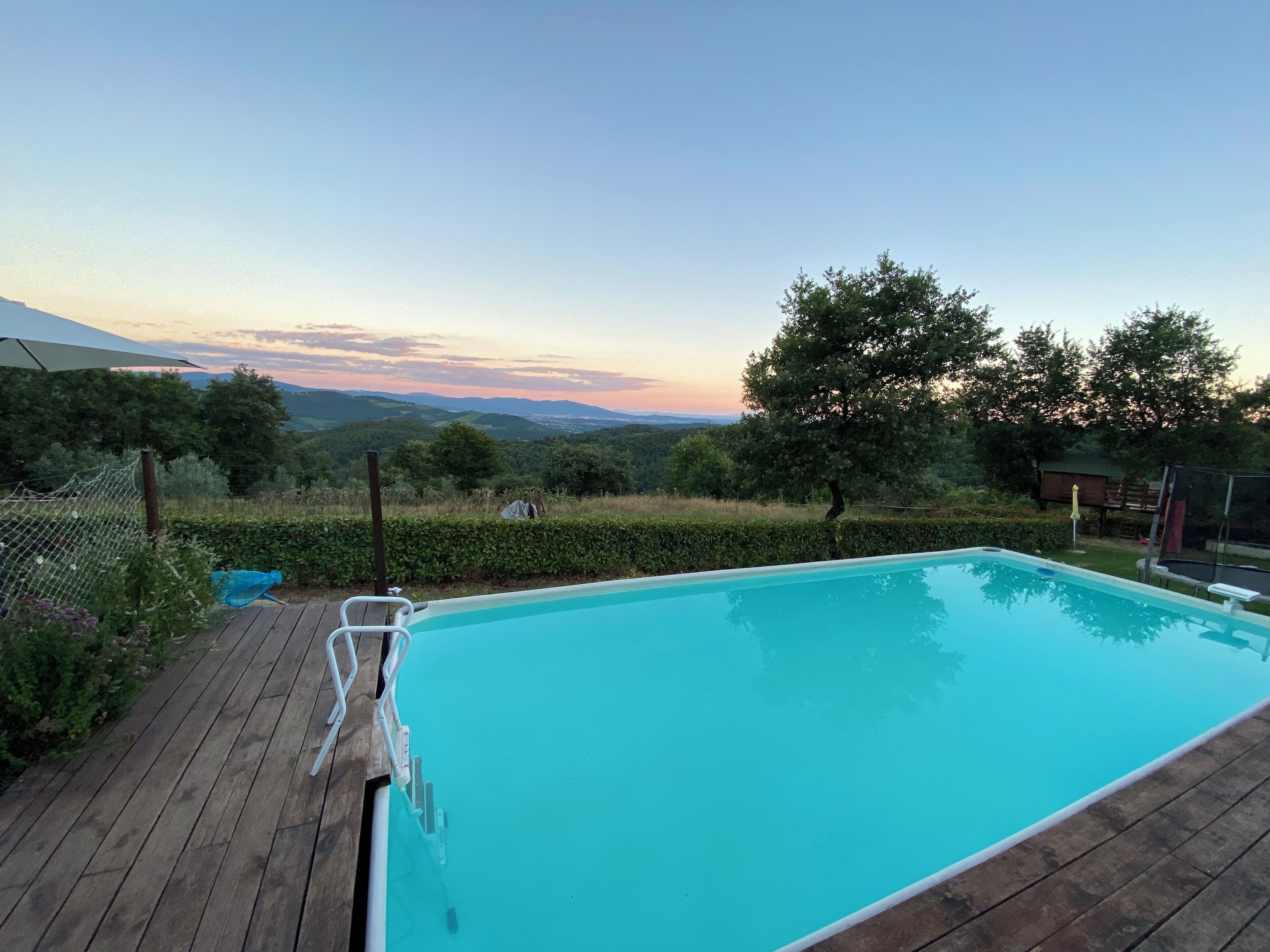 Una piscina con cubierta de madera, rodeada de vegetación y una vista panorámica de colinas.