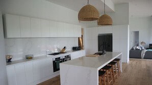 Een moderne keuken met witte kasten, een groot eiland met krukken, en een zithoek met een bank en kussens.