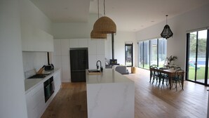 Een moderne keuken met een centraal eiland, houten vloeren en grote ramen met uitzicht op de omgeving.