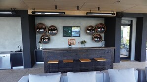 Een moderne bar met een houten toonbank, verschillende wijnflessen en een stadsgezichtschilderij aan de muur.