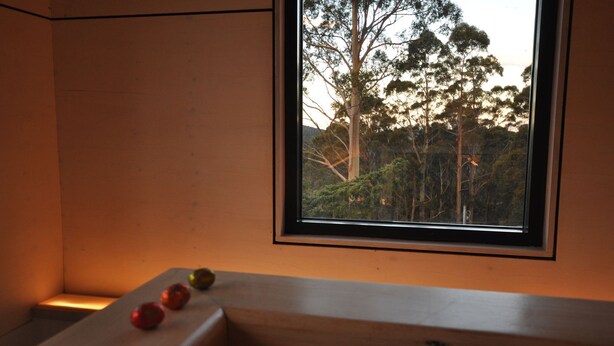 Una habitación con ventana que da a un bosque. Hay una pequeña mesa con algunas manzanas encima.