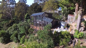 Una casa moderna de varios niveles con un amplio patio y paneles solares, rodeada de un bosque denso.