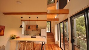 Una cocina moderna con vigas de madera, luces colgantes y vistas a un jardín exuberante a través de amplios ventanales.