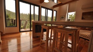 Una habitación amplia con ventanas grandes, suelo de madera y una zona de bar con taburetes.