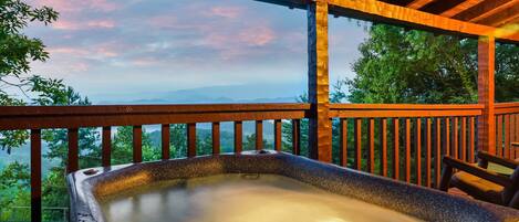 A hot tub on a wooden deck with a view of mountains and trees.
