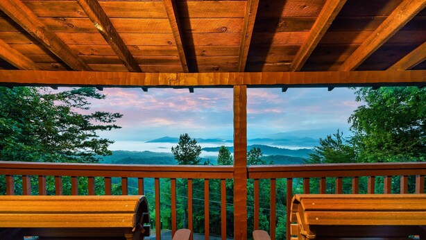 Una terraza de madera con dos sillas mirando un paisaje de montañas y árboles.