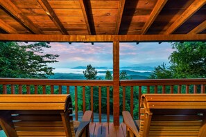 A wooden deck with two wooden chairs facing a scenic view of mountains and trees.
