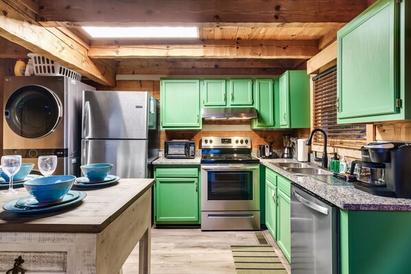 A modern kitchen with green cabinets, stainless steel appliances, and a wooden ceiling.