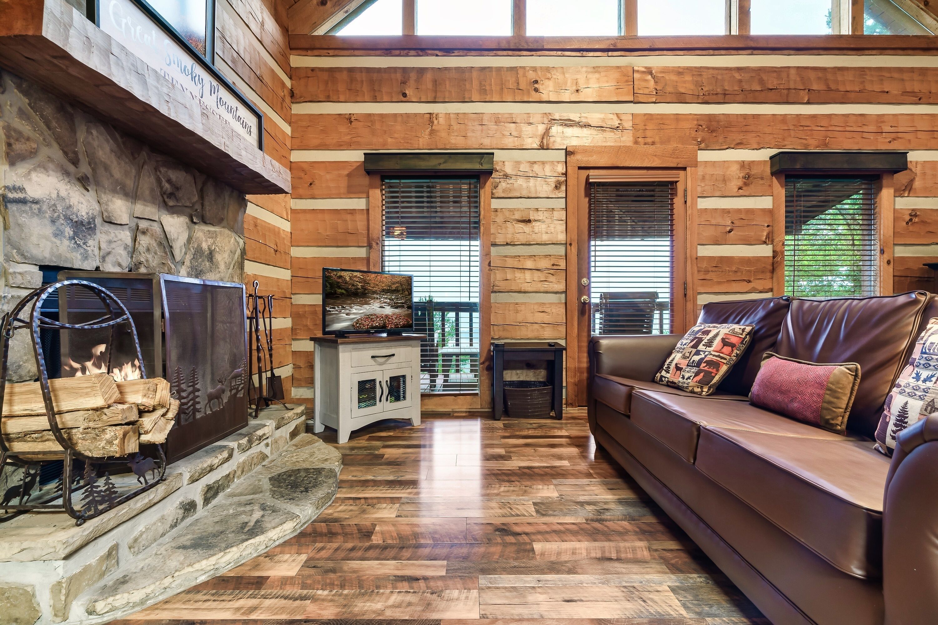 A log cabin interior with a stone fireplace, a leather sofa, and a wooden floor.