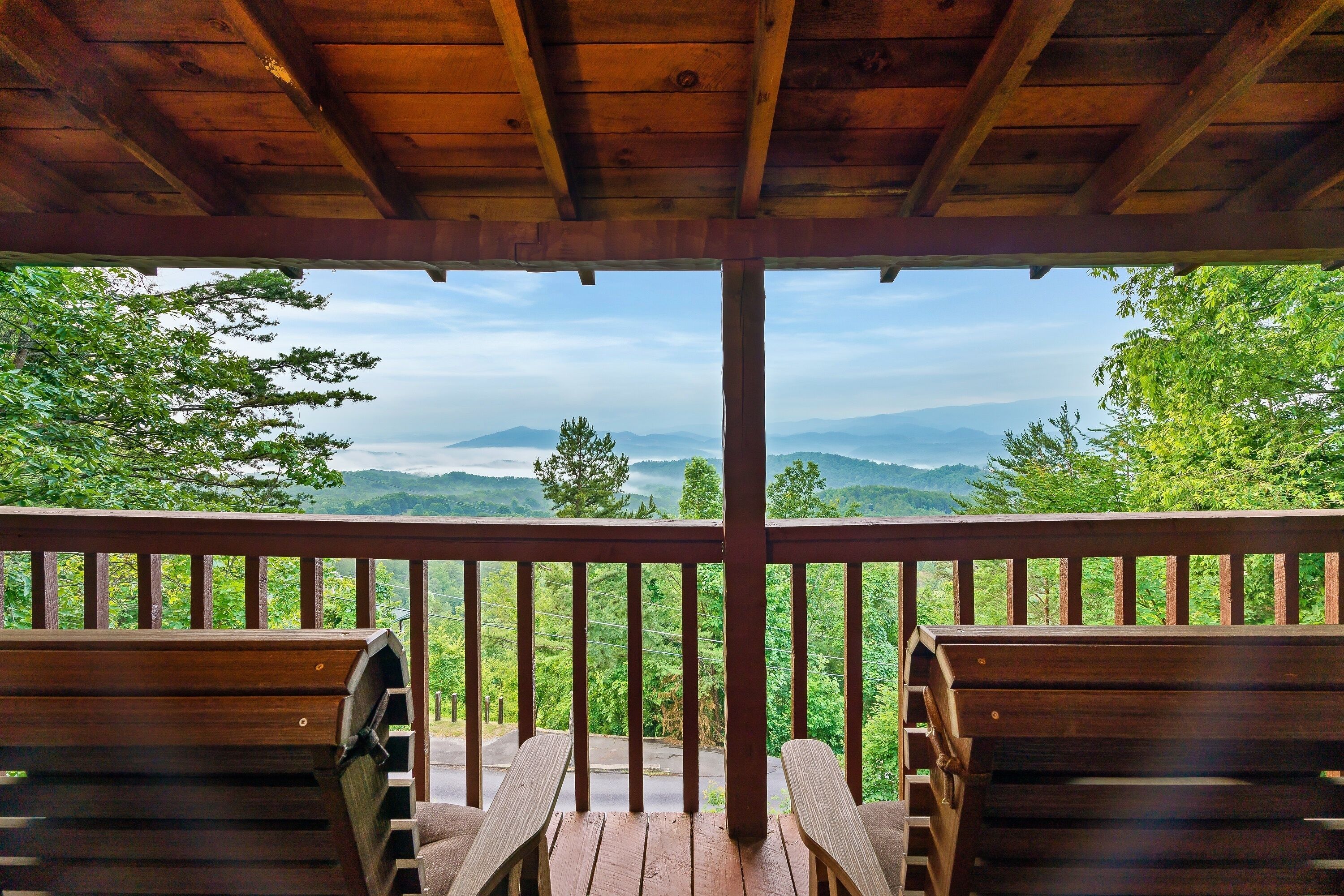 A wooden deck with two chairs facing a scenic view of mountains and greenery.