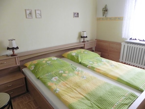 Une chambre avec deux lits simples, une tête de lit en bois, une table de chevet avec une lampe, une petite table et une chaise.