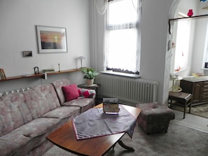 Un salon comprenant un canapé, une table basse, une petite table ronde avec une plante, un radiateur et une fenêtre avec des rideaux.