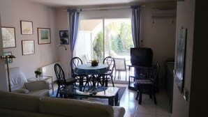 A living room with a sofa, a coffee table, a dining table with chairs, a television, and a view of the outdoors through a window. - ST RAFAEL-BOULOURIS, seaside, great appartment 2room, ground floor (St. Rafaël - Boulouris)