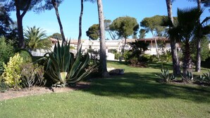 A well-maintained garden with various plants and trees, a paved pathway, and a building with a tiled roof in the background. - ST RAFAEL-BOULOURIS, seaside, great appartment 2room, ground floor (St. Rafaël - Boulouris)