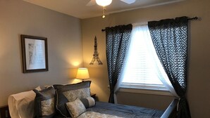 A bedroom with a bed, a nightstand, a lamp, a window with curtains, and a wall-mounted Eiffel Tower decoration. - Your Retreat in Austin - Relax & enjoy free Netflix movies Pet Stays for Free ! (Austin)