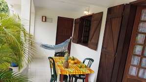 Un coin repas avec une table dressée pour quatre personnes, entourée de chaises, d’un hamac et d’une plante en pot.