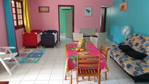 Une pièce comprenant une table à manger, des chaises, un canapé, une fenêtre avec des rideaux, une porte et un mur orné de tableaux.