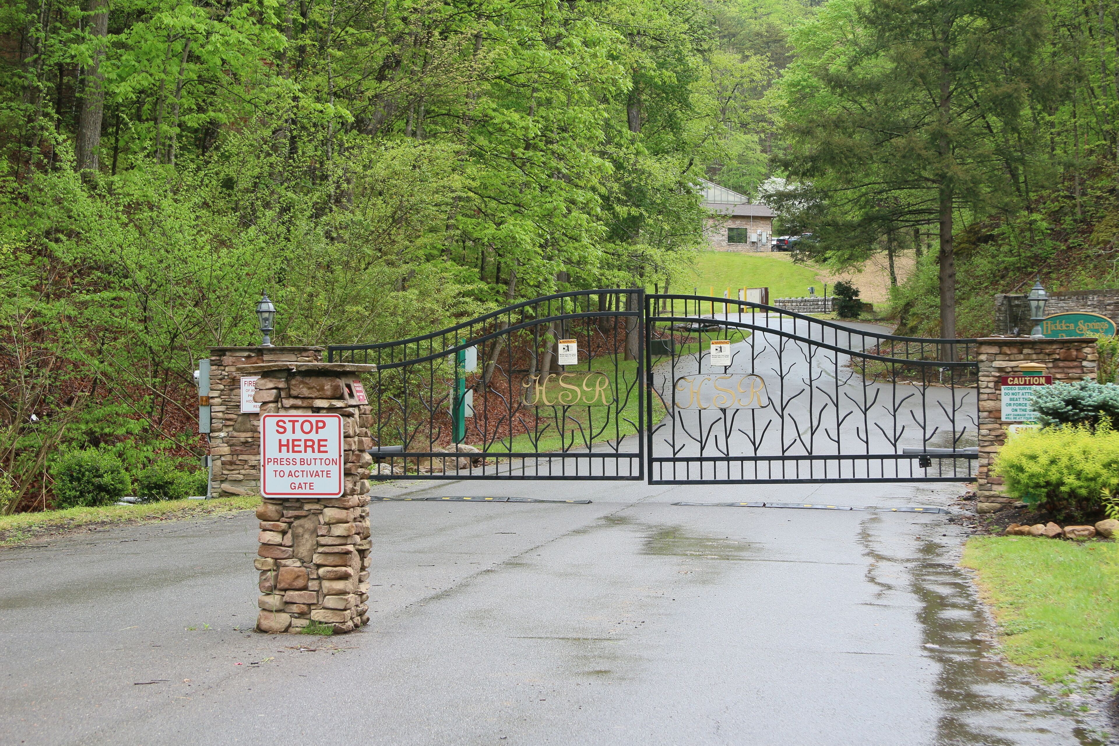 A gated entrance with a stone pillar and a stop button sign.