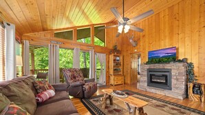 A wooden interior with a sofa, armchair, fireplace, and a television. - SR•Cozy Mountain Cabin• Private Hot Tub•1.5 Miles to Dollywood• Walk to the Pool (Sevierville)