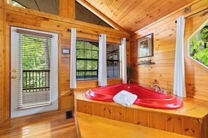 A wooden cabin with a red bathtub, wooden walls, and a window with blinds.