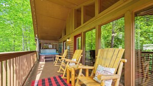 A covered porch with wooden chairs, a checkered mat, and a view of trees. - SR•Cozy Mountain Cabin• Private Hot Tub•1.5 Miles to Dollywood• Walk to the Pool (Sevierville)