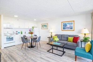 A modern living room with a grey sofa, a coffee table, and a dining area with a round table and chairs. - Waikiki condo w/ beach & resort access (Honolulu)
