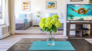 A living room with a wooden coffee table, a vase with yellow flowers, a TV, and artwork on the wall. - Waikiki condo w/ beach & pool access (Honolulu)