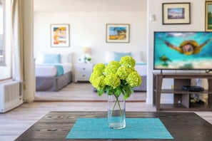 A living room with a wooden coffee table, a vase with yellow flowers, a TV, and artwork on the wall. - Waikiki condo w/ beach & resort access (Honolulu)