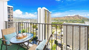 A balcony with a table and chairs, a view of a cityscape and mountains. - Waikiki condo w/ beach & pool access (Honolulu)