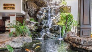 A waterfall feature with koi fish, surrounded by rocks and plants, and a sign indicating 'Tower I Makai'. - Waikiki condo w/ beach & pool access (Honolulu)