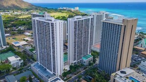A high-rise building complex with multiple floors, surrounded by greenery and a view of the ocean. - Waikiki condo w/ beach & pool access (Honolulu)