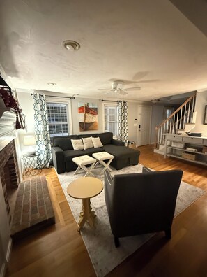 Ein Wohnzimmer mit einer Couch, einem Hocker und einem Sessel, einem Kamin und einer Treppe.