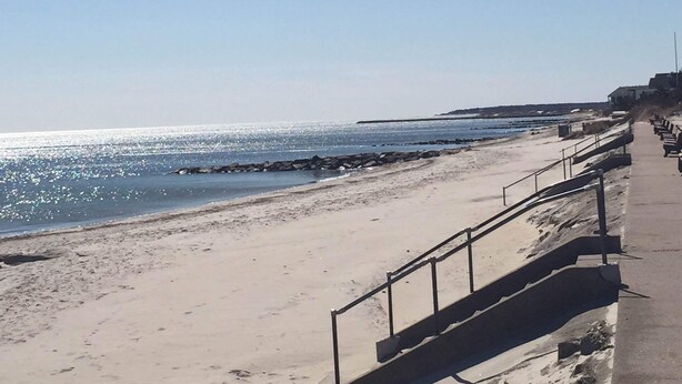 En strand med en gångbana av betong och bänkar längs strandkanten.