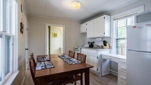 A compact kitchen with white cabinets, a dining table with placemats, and a refrigerator. - Salty Air Suites, B:  Easy to walk in, One level, 3 beds, ocean views. (Old Orchard Beach)