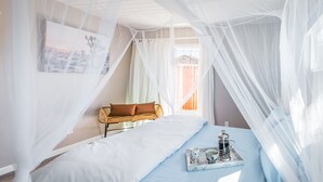 A bedroom with a bed, a bedside table with a tray, a chair, and a window with curtains.