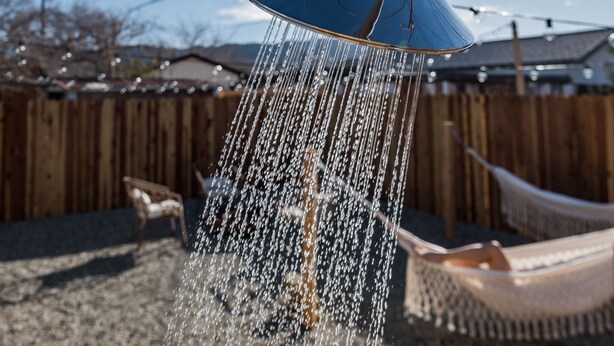 A blue water feature with water cascading down, set against a wooden fence and a hammock in a backyard.