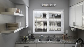 A kitchen with white cabinets, a granite countertop, a stainless steel sink, and a window with blinds.