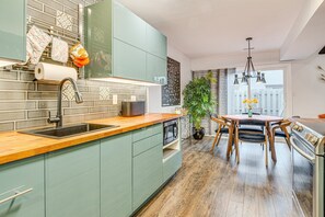 A modern kitchen with a wooden countertop, a built-in oven, and a sink. There is a dining area with a table and chairs, and a potted plant.