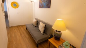 A room with a grey sofa, two pillows, a yellow mirror, a painting, a floor lamp, and a table with a lamp and a book. - ⭐ Best Location - 2 Bed + 2 Bath Private Apartment + WIFI (Chapinero)