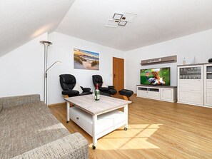 Een moderne woonkamer met een bank, twee zwarte leren fauteuils, een salontafel, een flatscreen-tv en een kast met glazen deuren.