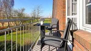 Un balcon avec une table et deux chaises, un mur en briques et une rambarde en métal.