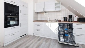 Une cuisine moderne avec des meubles blancs, un four encastré, un lave-vaisselle et une machine à café.