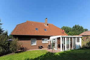 Een tweelaags huis met een rode pannendak, een overdekte patio en een kleine tuin.